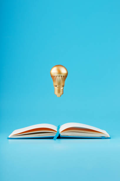 istock A gold-colored light bulb hangs above the blank pages of a notebook on a blue background. 1279166112