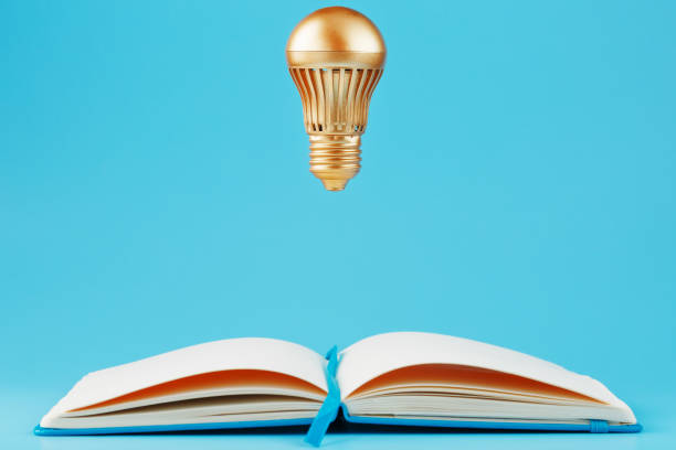 istock A gold-colored light bulb hangs above the blank pages of a notebook on a blue background. 1279166242