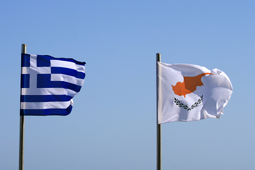 Greek and Cypriot national flags waving in front of blue sky