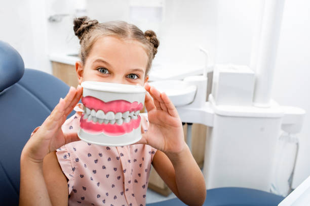 zahnpflege. emotionale kleine mädchen sitzt auf dem zahnarztstuhl und lächelnd - hygiene dental hygiene human teeth child stock-fotos und bilder