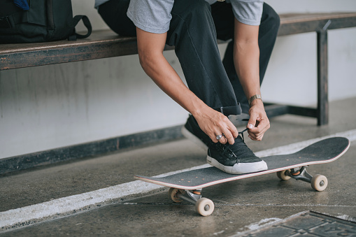 asian skateboarder tying his shoe before practicing skateboarding in the skateboarding park