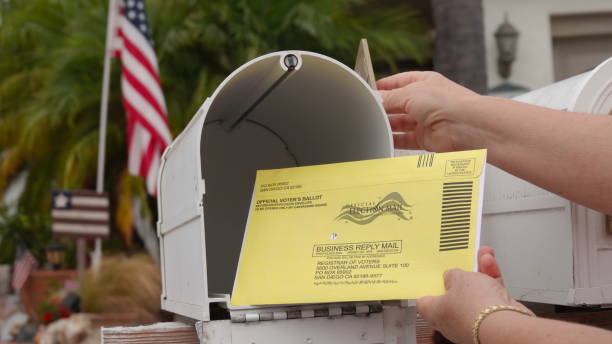 Woman puts US mail-in ballot into mailbox Close up of an American mailbox with flags in the background, older woman's hands returning mail-in election ballot. Illustrative editorial taken in Vista, CA / USA on October 8, 2020. absentee ballot photos stock pictures, royalty-free photos & images