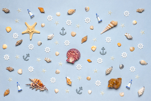 Various decorative nautical items, seashells, sea stars and miniature toys on blue pastel background. Sea travel, summer vacation at ocean concept. Flat lay, top view.