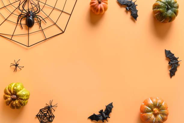 istock Halloween frame of fun party decorations, pumpkins, drinking straw, bat, skulls, spooky spider on orange background. Overhead view, flat lay. Copy space. 1279192155