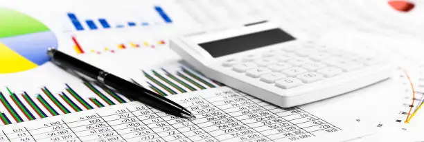 Photo of White calculator, coins and black pen on against the background of documents. Financial bookkeeping, Accounting Concept. Top view. Banner.
