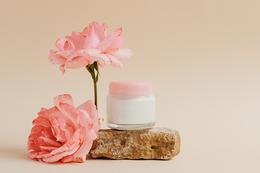 A jar of face or eye skin care cream on a piece of stone with rose flowers. The concept of natural cosmetics from natural materials, purity and tenderness. Copy space.