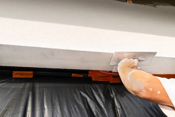 Photo of A construction worker applies and blurs a white layer of silicone plaster over the window jamb, the window is protected with foil.