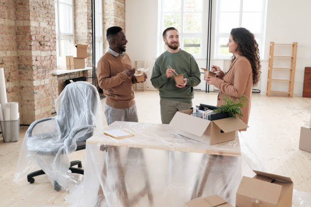 istock Team of young multi-ethnic coworkers standing at table covered with polyethylene and eating Chinese food while planning new startup project after moving into new office 1279200844