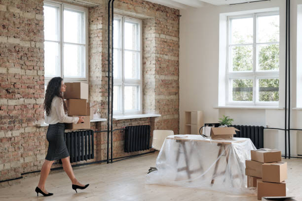 istock Modern young woman on heels carrying stack of moving boxes to table covered with polyethylene during relocation in new office 1279200916