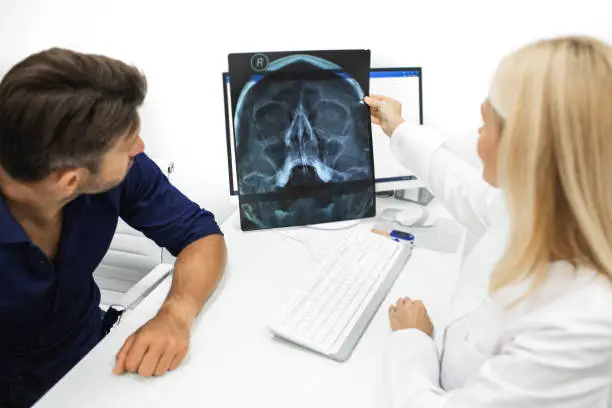 Physician showing a man patient an X-ray of her head and maxillary sinuses during a consultation. Diagnostics and treatment of sinusitis and frontal sinusitis