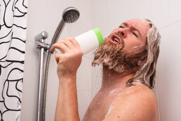 マイクの代わりにシャンプーボトルを使って自宅でシャワーを浴びながら歌うハンサムなひげを生やした男。幸せな白人の男は、人生を楽しんで表情で歌います。 - skin singer ストックフォトと画像