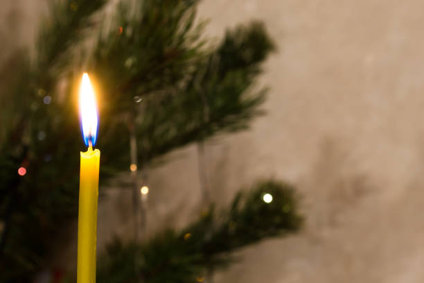 Close up color image depicting a lit red wax candle in the home at Christmas, surrounded by glowing Christmas lights (rendered into attractive bokeh circles) in the background. Room for copy space.