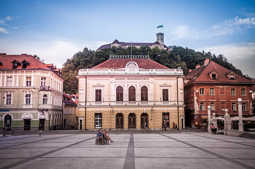 A young couple is sitting on the bench in front of the Slovenian Philharmonic Building at Congress Square (Slovene: Kongresni trg). The famous square is a pedestrian zone.