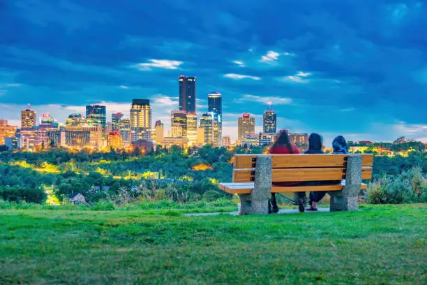 People relax on a park bench with the skyline of downtown Edmonton Alberta Canada in the background at twilight blue hour.