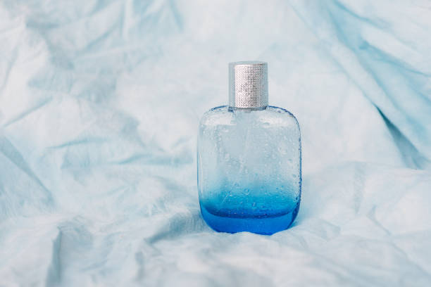 Close up of perfume bottle on blue textured background, tiny and delicate fabric with water drops. beauty concept. aroma of freshness
