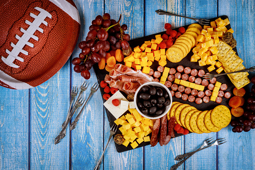 Football ball made from cheese and sausage for charcuterie board on wooden background. American football game concept.