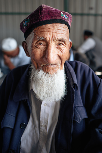A man wearing a Uyghur white hat and a white beard in Kuche, Xinjiang leaned on the table and smiled at the camera
