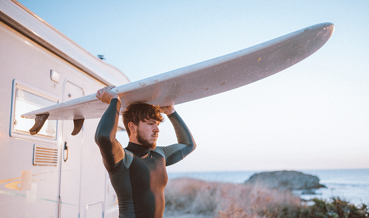 Portrait of male surfer carrying surfboard on head and looking at view on the beach at sunrise.