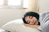 若い大人のアジアの女性は朝に寝室で眠る