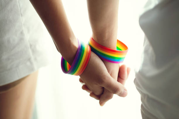 istock Closeup lesbian couple holding hands with a rainbow-patterned wristban on their wrists.Concept of LGBT, activism, community and freedom. 1279263474