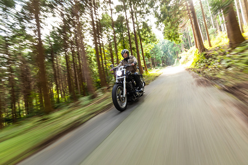 September/29/2020 at Gozaisho mountain forest road a man is riding his Harley Davidson motorbike. The trees and road have motion blur due to the slow shutter speed used.