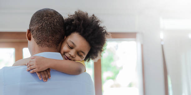 リビングルームで笑うアメリカのアフリカの父と息子の肖像画。幸せなパパと彼の小さな男の子は家で余暇を過ごす。シングルパパ、家族のライフスタイル父の日のコンセプトバナー - father son ethnic child ストックフォトと画像