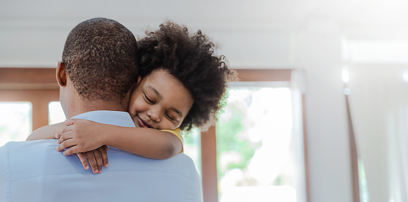 Portrait of american african father and son hugging laughing in living room. Happy daddy and his little boy spending leisure time at home. Single dad, family lifestyle father's day concept banner