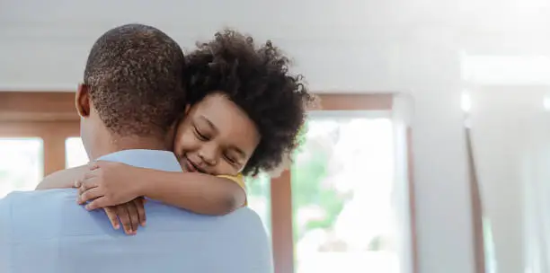 Photo of Portrait of american african father and son hugging laughing in living room. Happy daddy and his little boy spending leisure time at home. Single dad, family lifestyle father's day concept banner