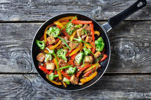 kung pao tofu with mixed peppers, broccoli and scallions in a skillet on a rustic wooden table, chinese cuisine, landscape view from above