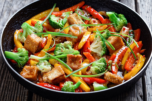 close-up of kung pao tofu with mixed peppers, broccoli and scallions in a skillet on a rustic wooden table, chinese cuisine, landscape view from above