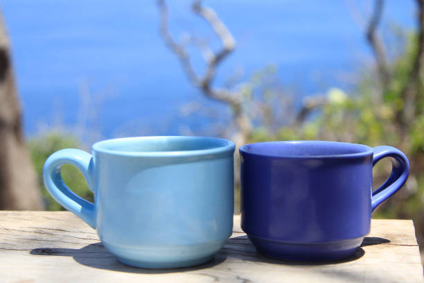 due tazze di caffè sul tavolo con sfondo spiaggia blu all'aperto. - morning coffee coffee cup two objects foto e immagini stock