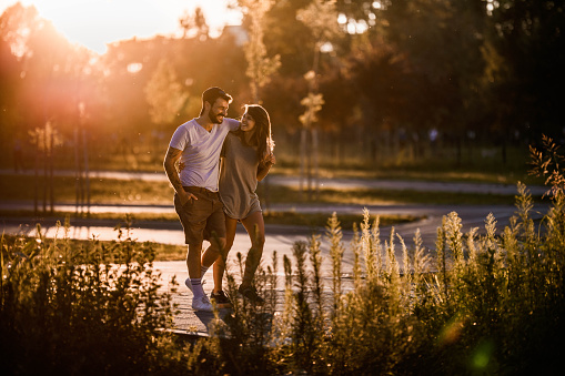 Happy couple enjoying in conversation while walking embraced in the park at sunset.