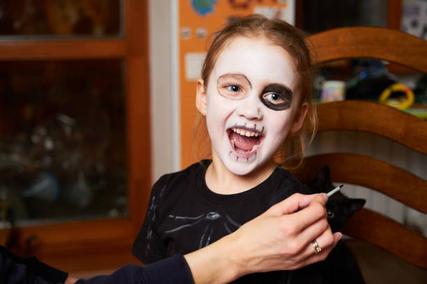 Mother is helping caucasuan daughter with Halloween makeup indoor. happy halloween