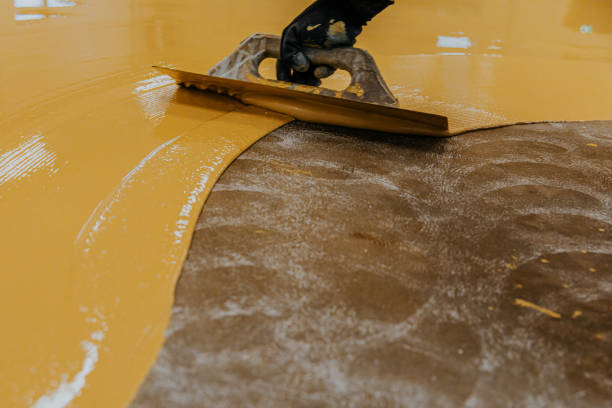 Worker, coating floor with self-leveling epoxy resin in industrial workshop.