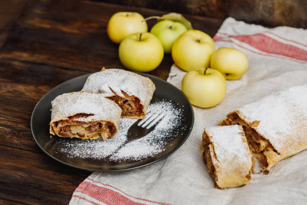 Apple strudel with icing sugar and raisins on black plate Apple strudel with icing sugar and raisins on black plate, wooden background apple strudel stock pictures, royalty-free photos & images