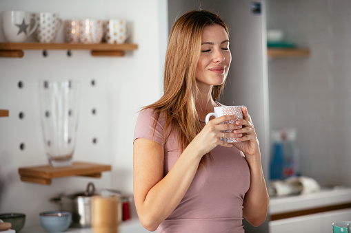 Young woman in kitchen. Beautiful woman preparing breakfast and drinking coffee