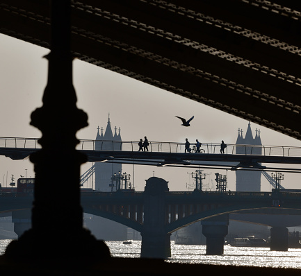 London bridges with distant figures in silhouette crossing the River Thames footbridge. View from the Embankment under and framing Blackfriars Railway bridge arch