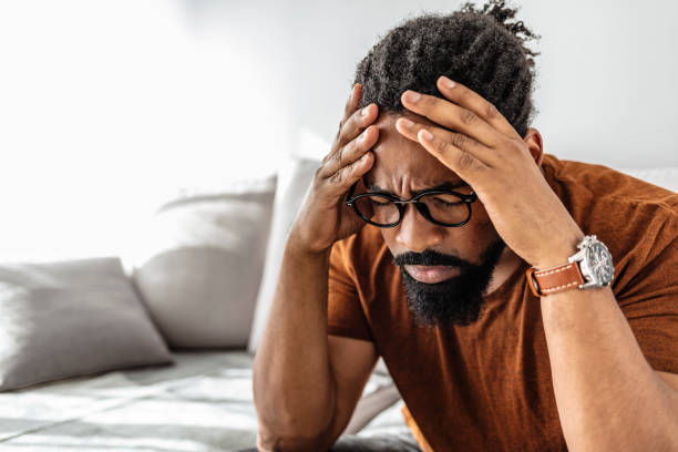 This is the worst headache I've had in a while Migraine. Afro Guy Having Headache Suffering From Pain Massaging Temples Sitting On Sofa At Home head in hands stock pictures, royalty-free photos & images