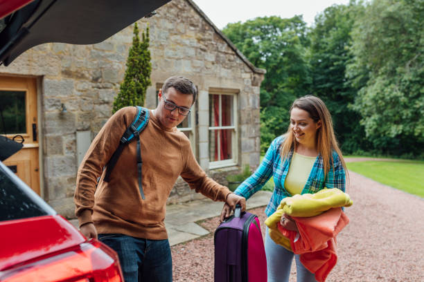 Help Me With This Please A shot of a young man and woman unpacking suitcases from a car. They are all wearing casual clothing and are outside a country home. staycation stock pictures, royalty-free photos & images