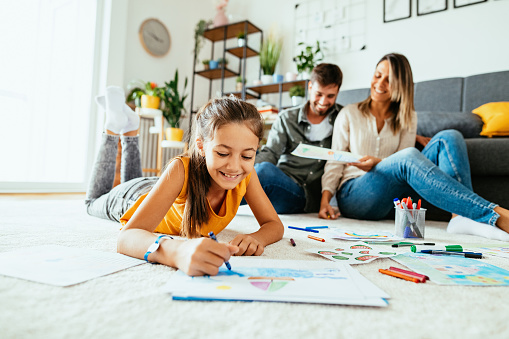 Parents expressing happiness while daughter drawing with crayons and pencils memories from vacations