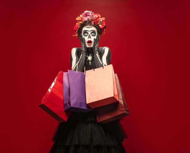 Young girl in the image of Santa Muerte, Saint death or Sugar skull with bright make-up. Portrait isolated on studio background. Shopping. Young girl like Santa Muerte Saint death or Sugar skull with bright make-up. Portrait isolated on red studio background with copyspace. Celebrating Halloween or Day of the dead. Black friday. muerte stock pictures, royalty-free photos & images