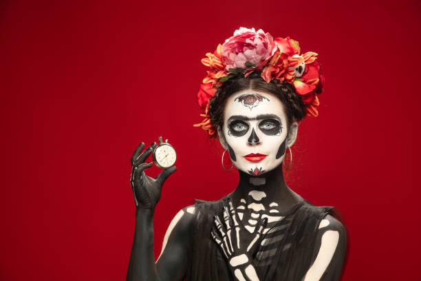 Young girl in the image of Santa Muerte, Saint death or Sugar skull with bright make-up. Portrait isolated on studio background. Hurry up. Young girl like Santa Muerte Saint death or Sugar skull with bright make-up. Portrait isolated on red studio background with copyspace. Celebrating Halloween or Day of the dead. Sales muerte stock pictures, royalty-free photos & images