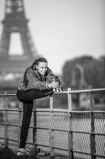 Young woman tourist exercising near river Seine with Eiffel tower on the background. Rain drops is visible