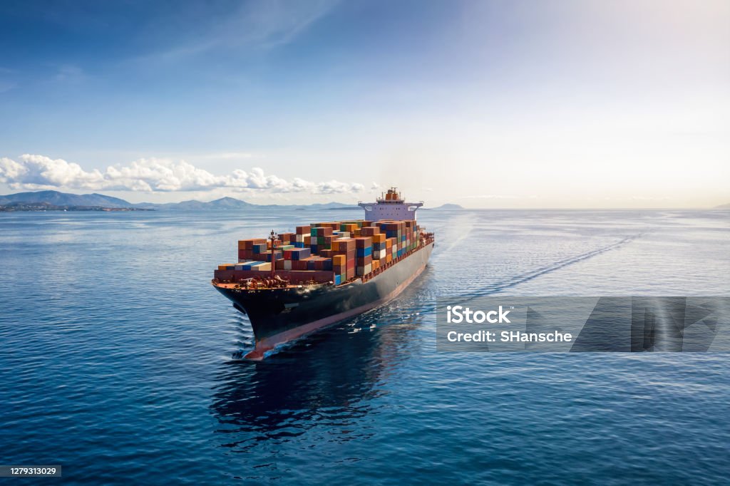 Aerial view of a heavy loaded container cargo vessel Aerial view of a heavy loaded container cargo vessel traveling over calm, blue sea Freight Transportation Stock Photo
