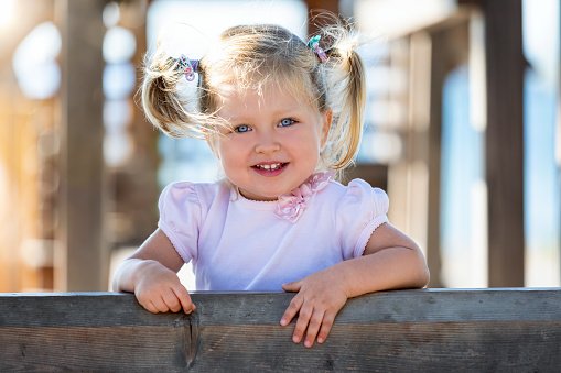 Portrait of a cute, blue eyed baby girl with pigtails in her hair on an outdoor playground in the park
