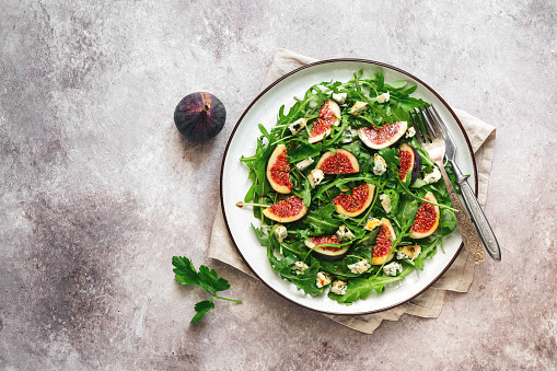 Fresh diet salad figs, arugula and blue cheese in a plate on a rustic beige background. Vegan and vegetarian lunch or dinner. Top view, flat lay, copy space