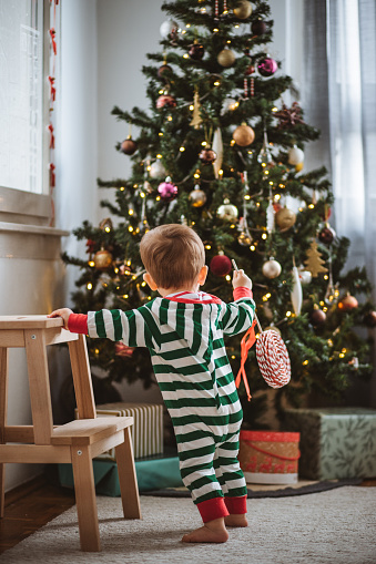 Toddler boy enjoying in Christmas morning. He is playing with decoration and gifts.