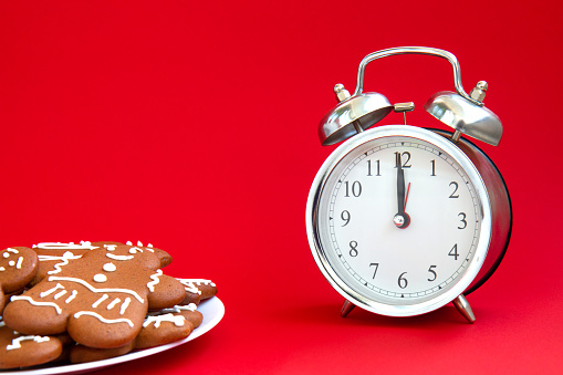 Beautiful vintage silver alarm clock and a plate of gingerbread cookies on a bright red background. Time concept. Holiday routine. Waiting for the holiday