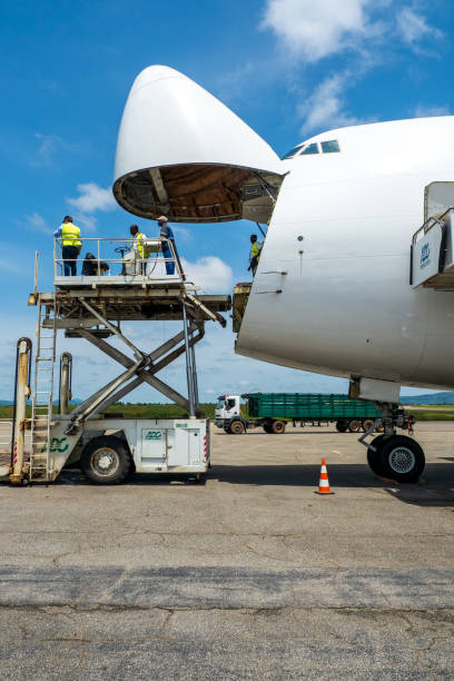 ein boeing 747 jumbo jet frachtflugzeug mit einer weit geöffneten nasenladetür wird von einem hochlader an einer frachtrampe abgeladen - window cockpit boeing 747 commercial airplane stock-fotos und bilder