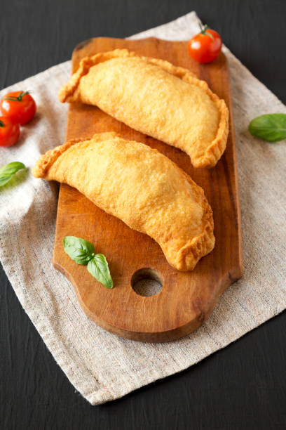istock Homemade Deep Fried Italian Panzerotti Calzone on a rustic wooden board on a black surface, low angle view. Close-up. 1279320122